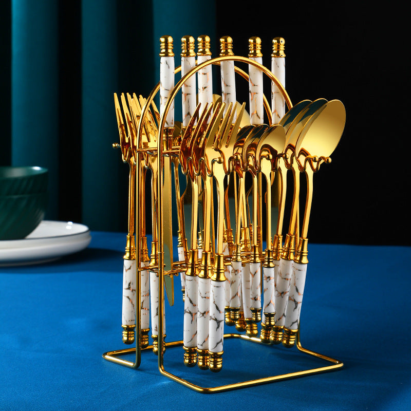 Ensemble de couverts dorés avec poignées blanches, présenté sur un support, pour une table élégante.