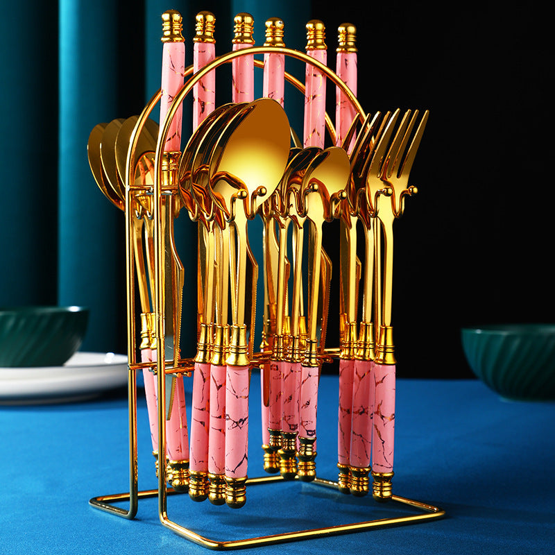 Ensemble de couverts en or avec poignées roses, présenté sur un support élégant sur une table moderne.