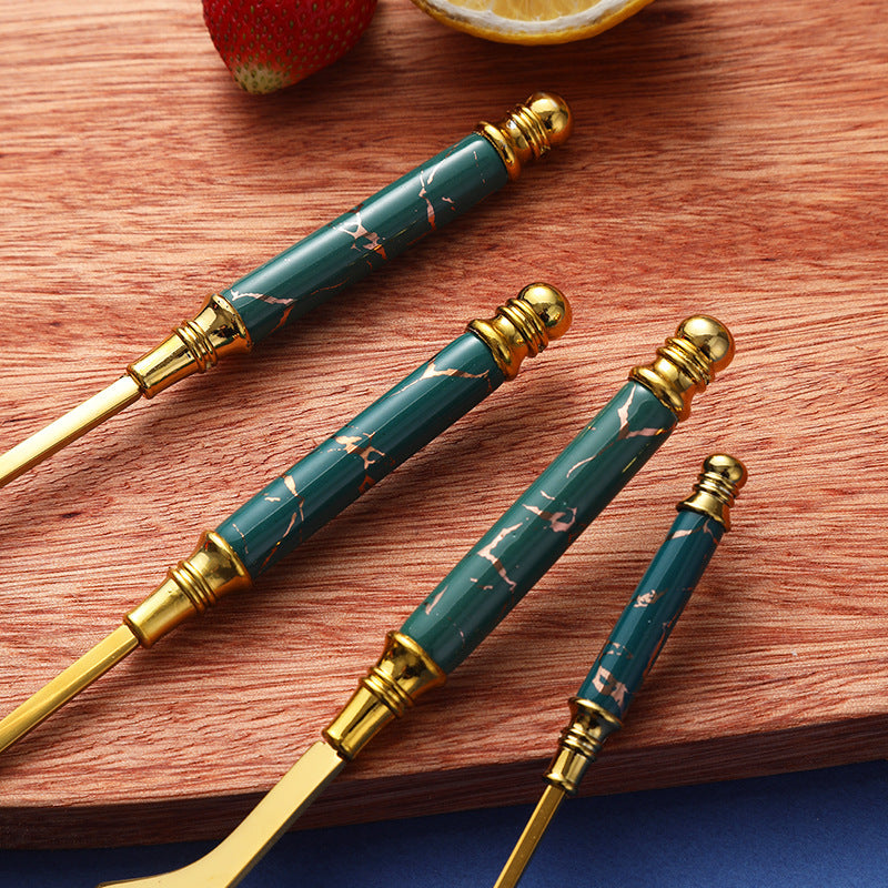 Set of elegant green and gold stainless steel cutlery on a wooden board, featuring marbled handles.