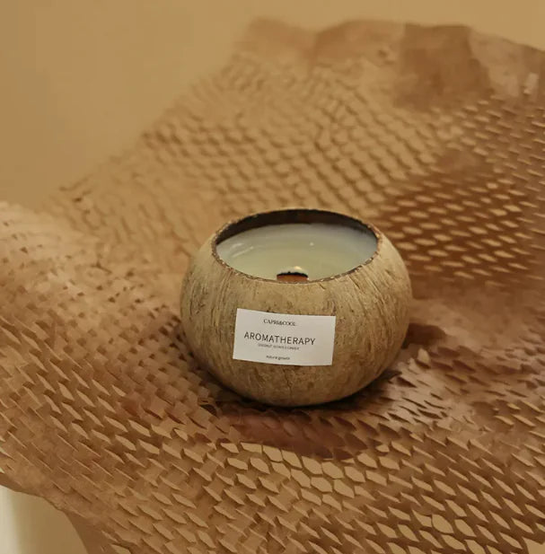 Bougie parfumée à la noix de coco dans un contenant en noix, sur fond de papier texturé.